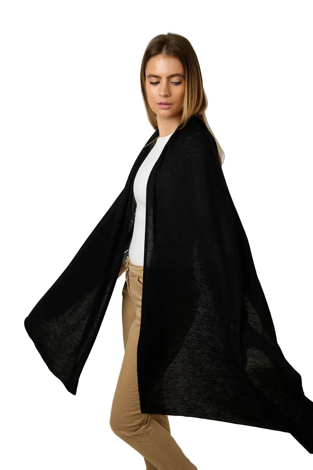 A woman modeling a lightweight black open-front shawl or wrap over a white top and tan pants, photographed against a plain light gray studio background.