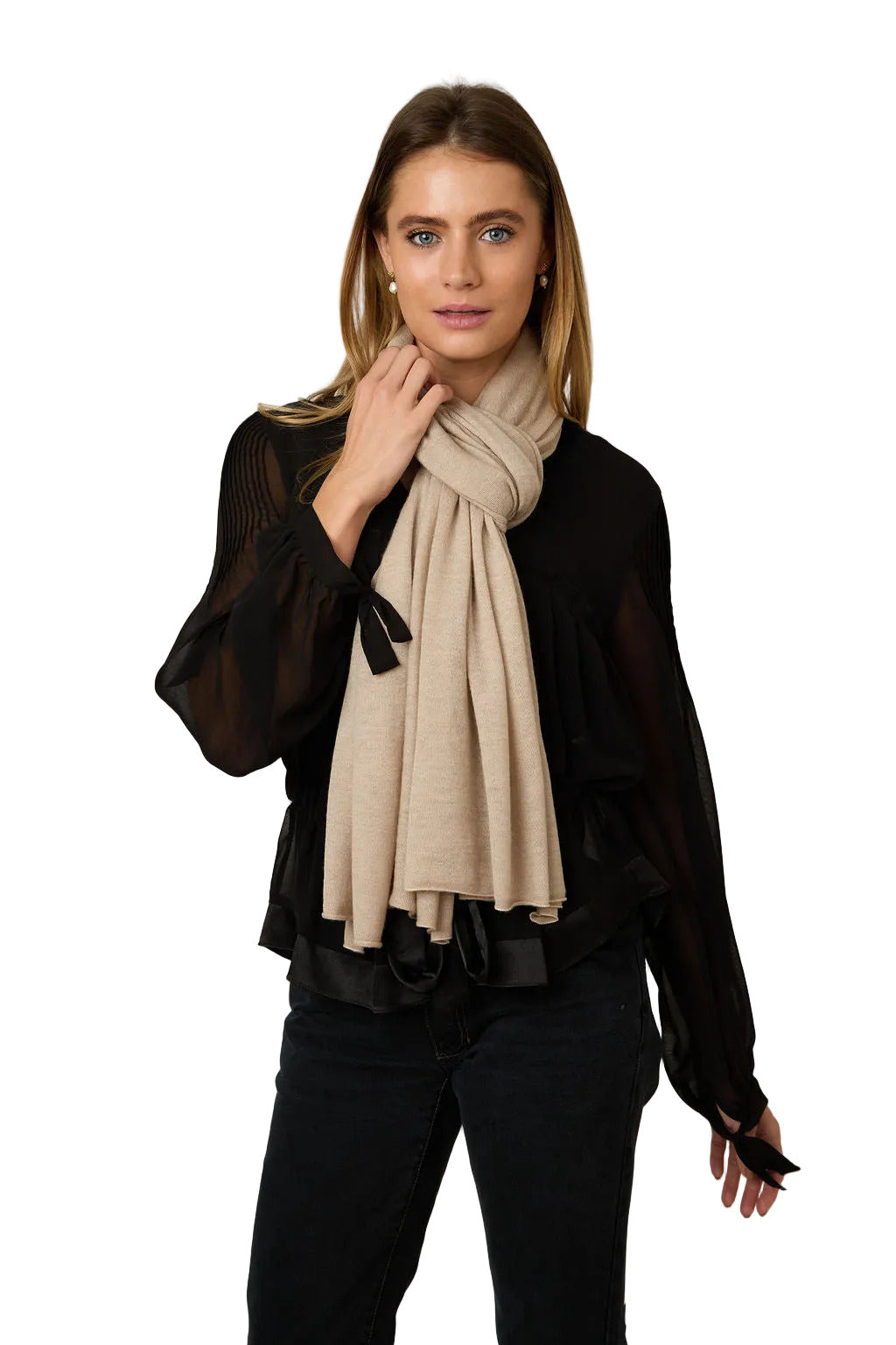 A woman modeling a light beige knit scarf wrapped around her neck, paired with a sheer black long-sleeve blouse and black pants, against a plain light gray studio background.