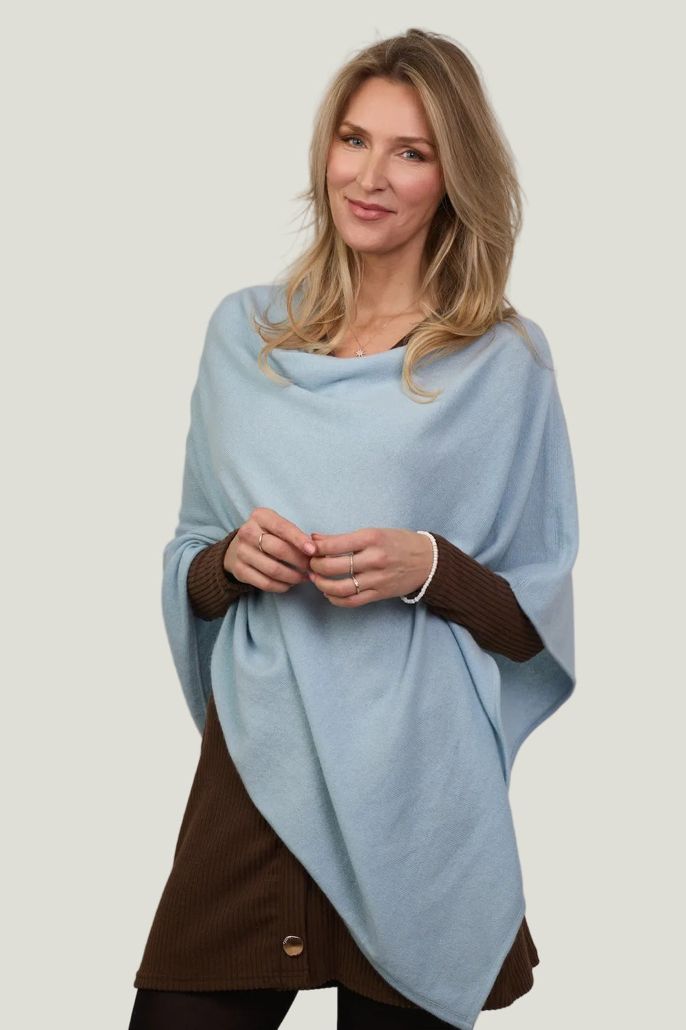 Woman wearing a light blue poncho over a brown outfit against a plain background