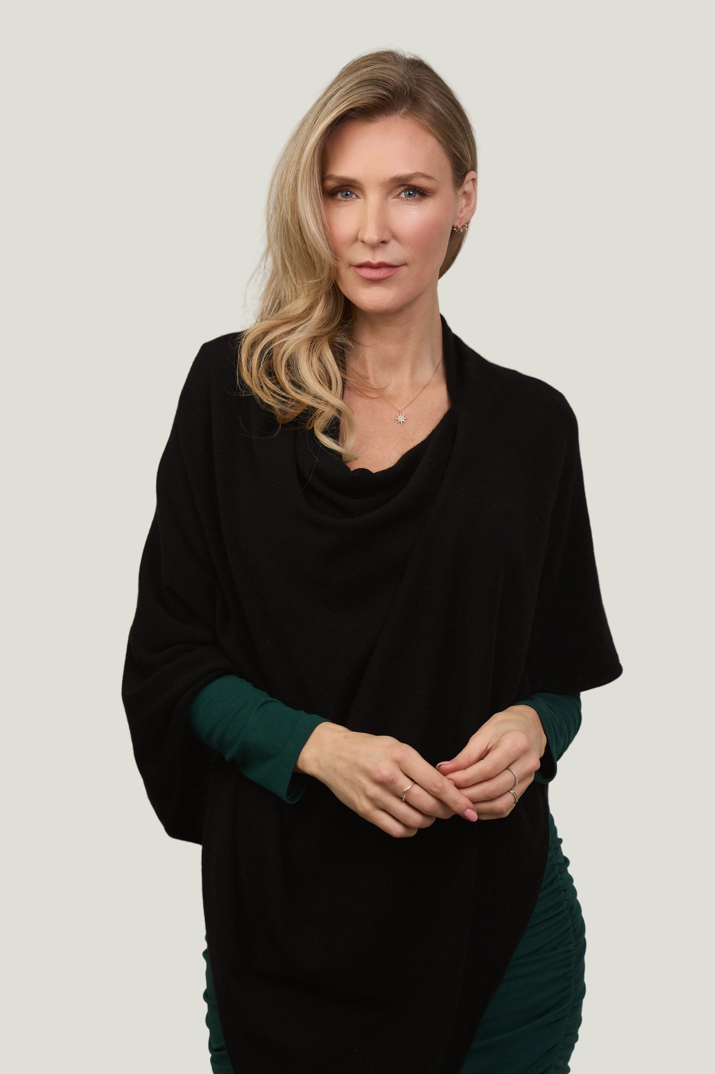 Woman wearing a black poncho over a green dress against a plain background