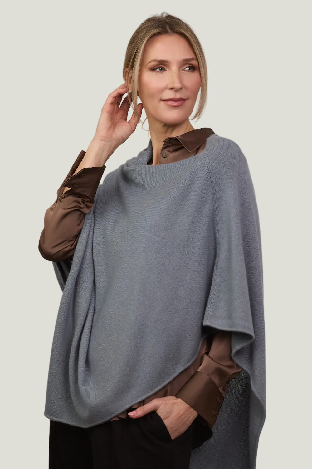 Woman wearing a ocean gray poncho over a brown shirt on a plain background