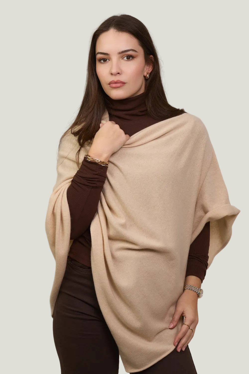 Woman wearing a beige poncho over a brown outfit against a plain background